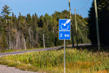 Trash symbol on a blue road sign after 2 km, pine trees forest on the roadsides, Canadian rural...