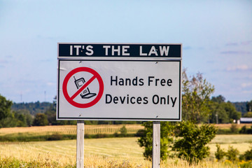 It's the law, hands free device only with no mobile symbol., Information Road white Sign on Canadian rural country roadside against prairies, plains