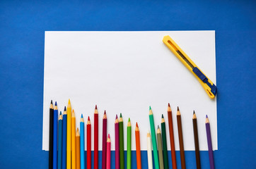 Color pencils and white sheet of paper on a blue background