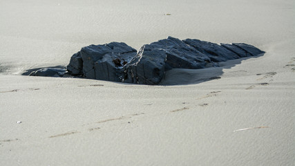 Rock boulder revealed by waves beach sand .