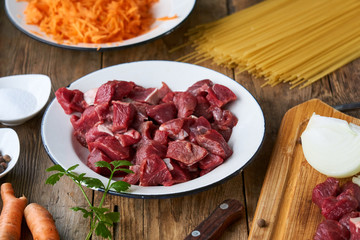 Pieces of raw beef in a white bowl on a wooden background
