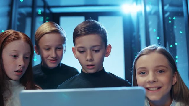 Young boy prodigy programming on laptop computer in server cabinet. Curious group of kids looking at monitor with excitement learning computer science. Smart generation concept.
