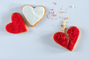 Three heart shaped red and white cookies, one is broken on white background, concept of jealousy, cheating breaking, ending relationships, unrequited love