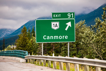 Information road green sign, the next exit after 91 km, Canmore, 1A road symbol, Canadian rural roadside forests in the background, Alberta, Canada