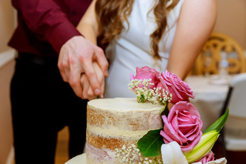 Obraz na płótnie Canvas Groom and bride cut naked wedding cake on wedding banquet with purple rose.