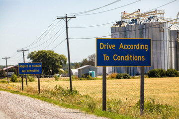 French, English Information road Signs, Drive According To Conditions. Canadian rural country roadside, grain silos in the background, Ontario Canada - obrazy, fototapety, plakaty