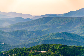 Layers of mountains in the haze during sunset. Beautiful sunset in the mountains. Beautiful sunset in a hilly valley with villages and fog in the lowlands.