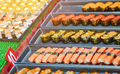 Rows of japanese sushi food. Maki ands rolls with tuna, salmon, shrimp, crab and avocado. Top view of assorted sushi in black plastic container being sale at market. Selective focus.