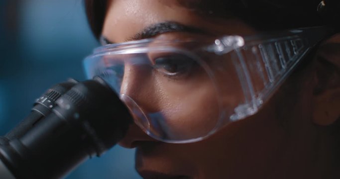 Close Up Of A Female Research Scientist Eyes, Looking At Samples Under Microscope, Wearing Safety Glasses.Slow Motion, Slider, Shot With BMPCC 4K.Biochemistry, Pharmaceutical Medicine,science