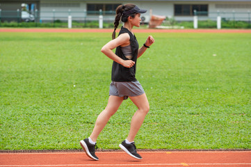 Side view of young athlete runner woman running in the running track in stadium. Running track is a rubberized artificial running surface for track and field athletics.