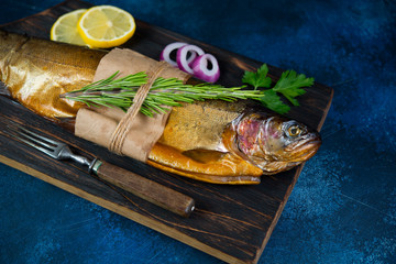 Hot smoked trout lie on a wooden chopping Board with lemon, onions and fresh herbs. Horizontal...