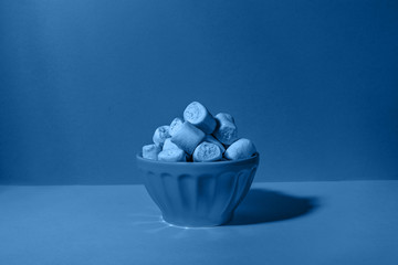 Bowl of giant marshmallows on solid backdrop with harsh shadows, toned in classic blue