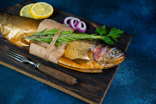 Hot smoked trout lie on a wooden chopping Board with lemon, onions and fresh herbs. Horizontal photo.