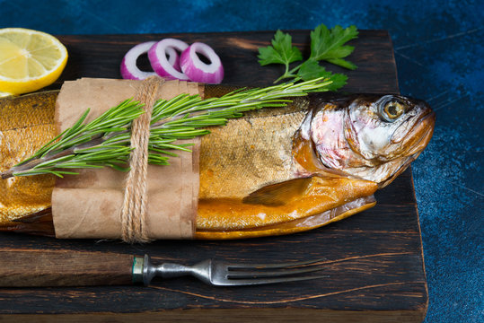 Hot smoked trout lie on a wooden chopping Board with lemon, onions and fresh herbs. Horizontal photo.