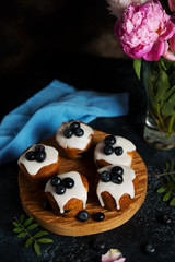 Still life of delicious homemade muffins poured with sugar Fudge and decorated with blueberries on a dark background.