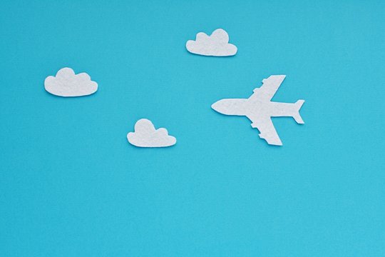 Travel, journey concept. Airplane and white clouds made from felt fabric on blue background.