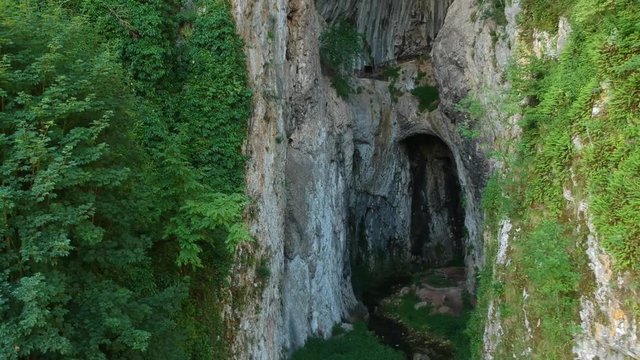 Cliff of Dreznicka Gradina Mountain with the monumental entrance into the Potpec Cave, drone dolly in shot