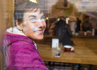A smiling girl sits in a coffee shop and looks out the window.