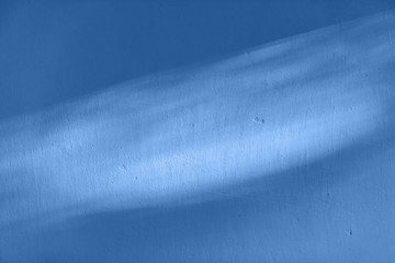 Ray of light on textured wall in classic blue color.