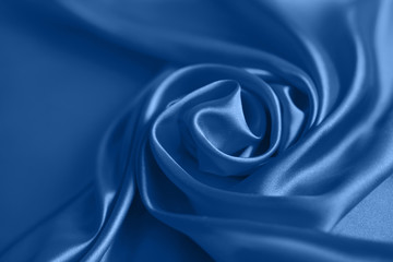 Close up of ripplesin shape of rose flower in blue silk fabric. Satin textile background.