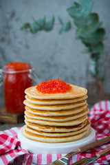 A tower of American pancake with red caviar stands on a wooden gray background. Vertical photo.