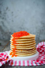 A tower of American pancake with red caviar stands on a wooden gray background. Vertical photo.