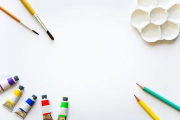 top view of brushes, color tubes, pencils and palette on white drawing pad background, copy space,...