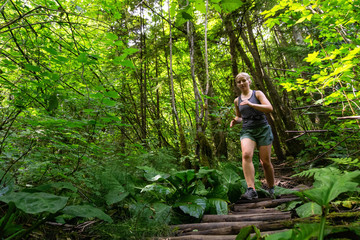Naklejka na ściany i meble Adventurous Girl Trail Running in the Woods during a vibrant summer day. Taken in Deep Cove, North Vancouver, British Columbia, Canada.