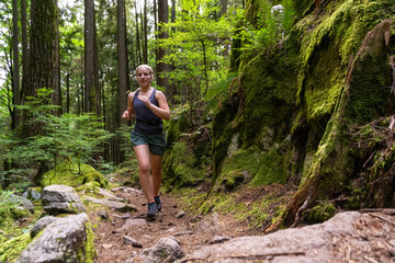 Adventurous Girl Trail Running in the Woods during a vibrant summer day. Taken in Deep Cove, North...