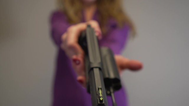 View looking down the barrel of a large black handgun pointed by woman