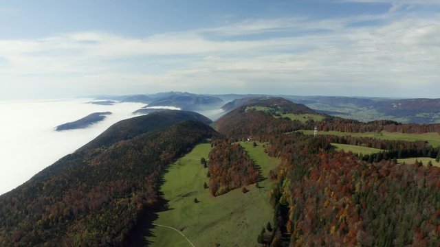 Epic aerial footage of autumn colored forest covered mountains at Grenchenberg in Switzerland with a sea of fog below in the valley
