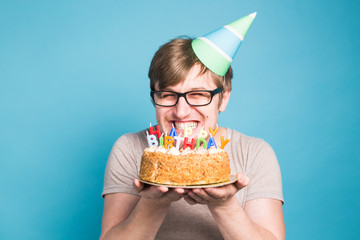Crazy funny young man in glasses and paper congratulatory hats holding cakes happy birthday standing on a blue background with copyspace