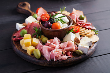 Antipasto platter with ham, prosciutto, salami, cheese,  crackers and olives on a wooden...