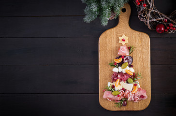 Antipasto platter with ham, prosciutto, salami, cheese and olives on a wooden background.  Christmas table. Top view, overhead