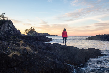 Obraz premium Wild Pacifc Trail, Ucluelet, Vancouver Island, BC, Canada. Girl Enjoyin the Beautiful View of the Rocky Ocean Coast during a colorful and vibrant morning sunrise.