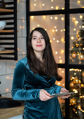 A young woman in the kitchen with a tablet in the kitchen. Christmas background-lights.