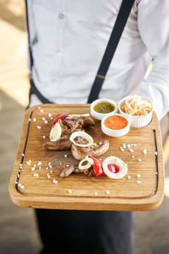 The waiter is holding a plate of Lamb tongue kebab with Pickled cabbage and two sauces. Serving on a wooden Board. Barbecue restaurant menu, a series of photos of different meats.