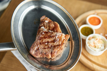 The waiter is holding a plate Grilled striploin steak with Pickled cabbage and two sauces. The strip steak, also called a New York strip. Serving on a wooden Board. Barbecue restaurant menu.