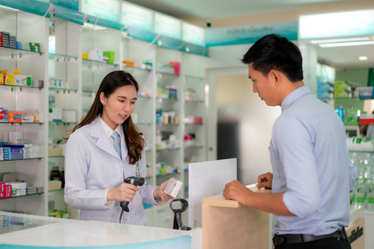 Confident Asian Young Female Pharmacist With A Lovely Friendly Smile Scan Bar Code In Medicine Box In The Pharmacy Drugstore. Medicine, Pharmaceutics, Health Care And People Concept.