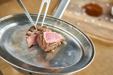 The waiter is butchering griled meat with a knife. Fried dry aged beef fillet chateaubriand medallion steak natural with Pickled cabbage and two sauces. Barbecue restaurant menu.
