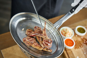 The waiter is butchering with a knife. Rack of lamb , grilled meat with bone. Barbecue restaurant menu, a series of photos of different meats