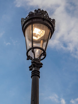 Street lamp in paris, shining against a blue sky with clouds