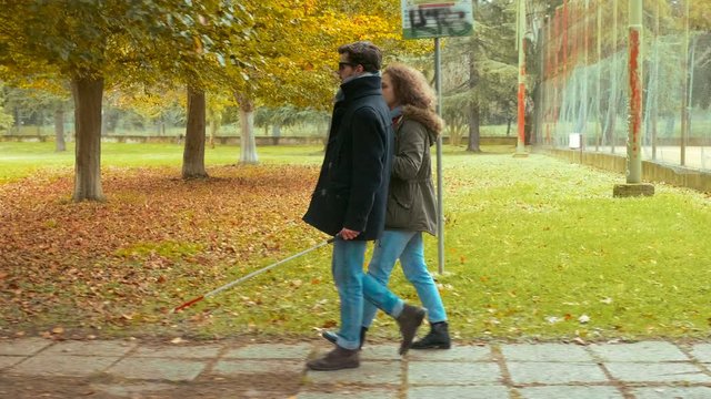 young blind man walking at the park with his girlfriend arm in arm
