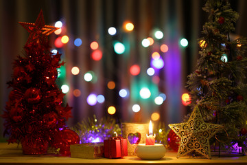 Fototapeta na wymiar Lit red candle light and gift box with Christmas tree and golden stars cenic on wooden table and colorful bokeh background 
