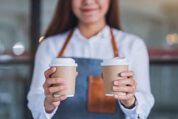 A waitress holding and serving two paper cups of hot coffee in cafe