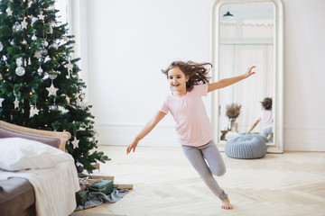 Girl runs around the room decorated for the new year, Christmas tree