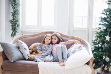 Obraz premium Two girls, sisters sitting on the couch, waiting for the holiday, the room is decorated for the new year and Christmas