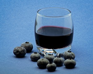 Glass of red wine with blueberries on blue background