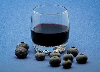Glass of red wine with blueberries on blue background