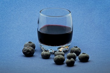 Glass of red wine with blueberries on blue background